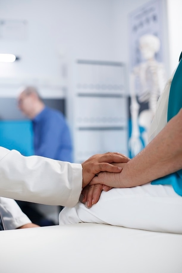 A nephrologist resting a hand on a patient's hand at the bedside